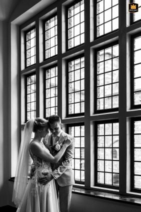   At Kasteel Helmond, the bride and groom share an intimate session by tall, grid-patterned windows, their foreheads nearly touching as daylight streams in from the side.